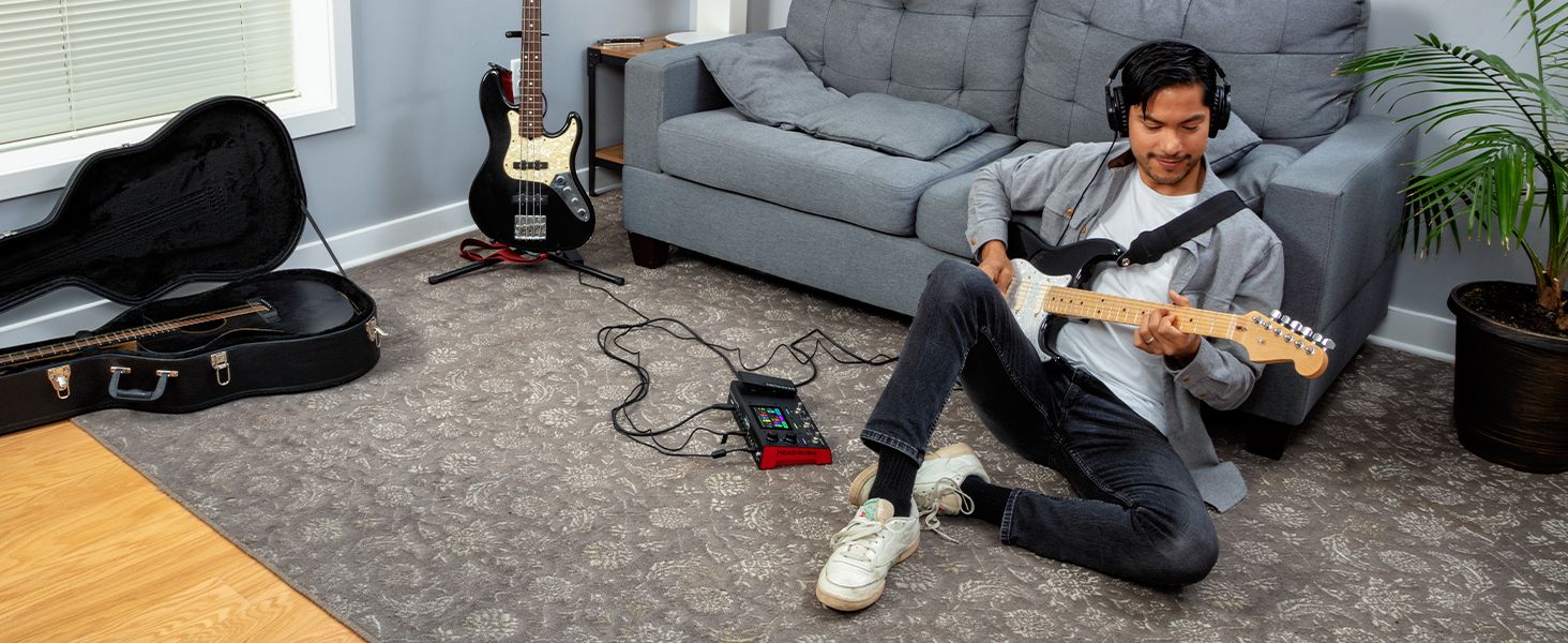 a man sitting on the floor  playing on a guitar with headphones on that are connected to the MX5 
