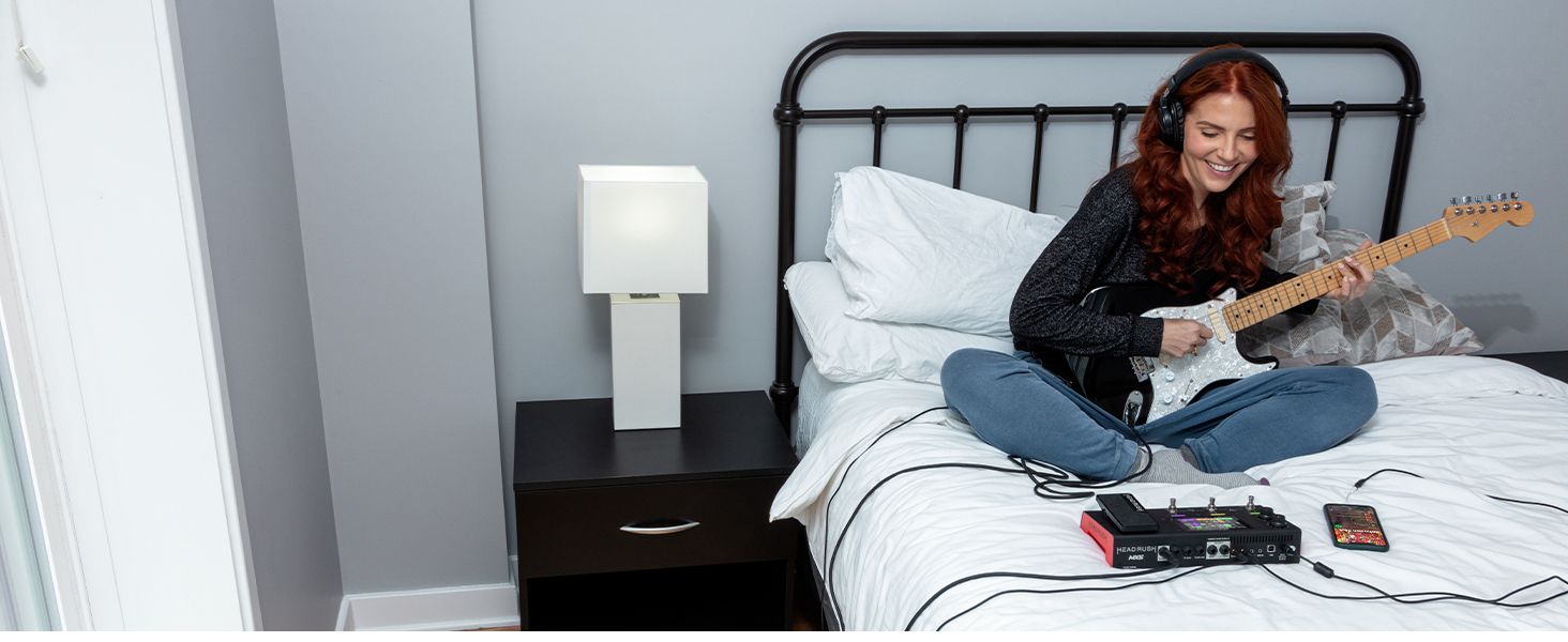 a girl sitting on a bed playing on guitar with headphones on and her phone is connected to the MX5