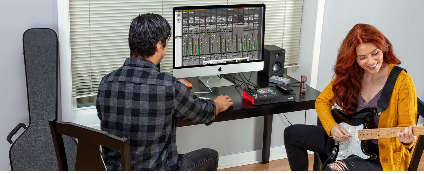 a man on a PC that is connected to the MX5 and a woman playing on the guitar 