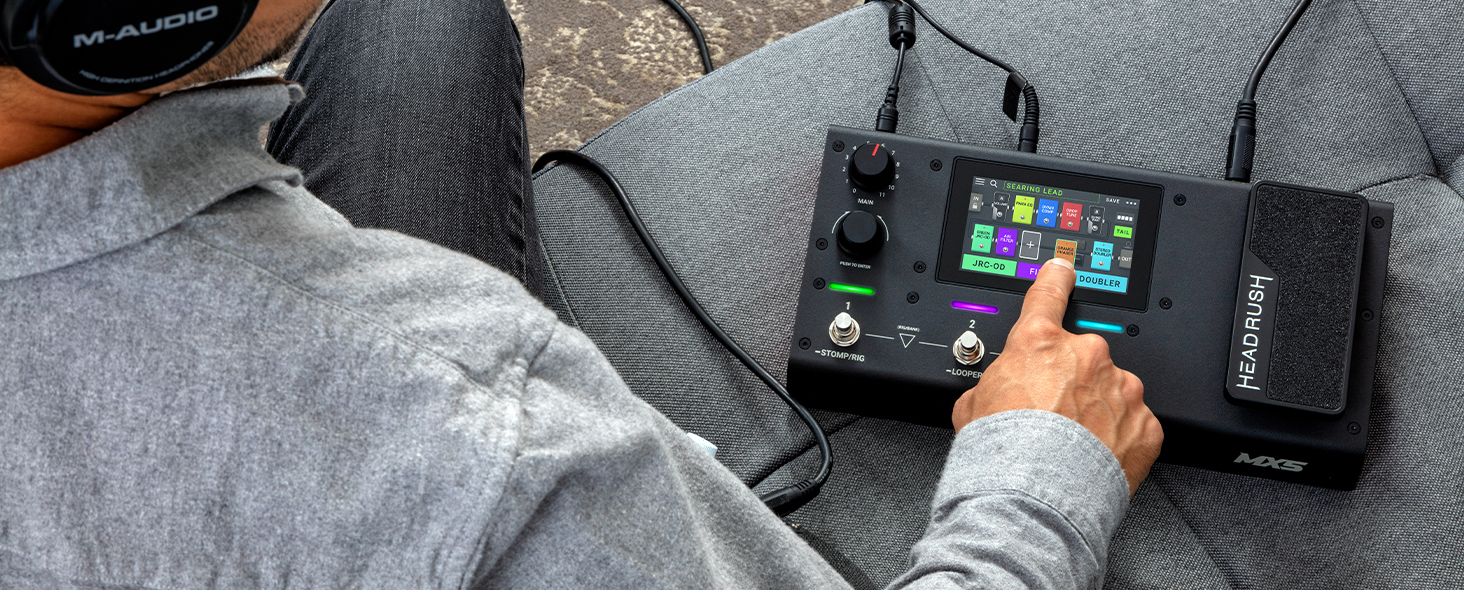 a man with headphones on sitting on a couch , using the touch display on the Headrush MX5