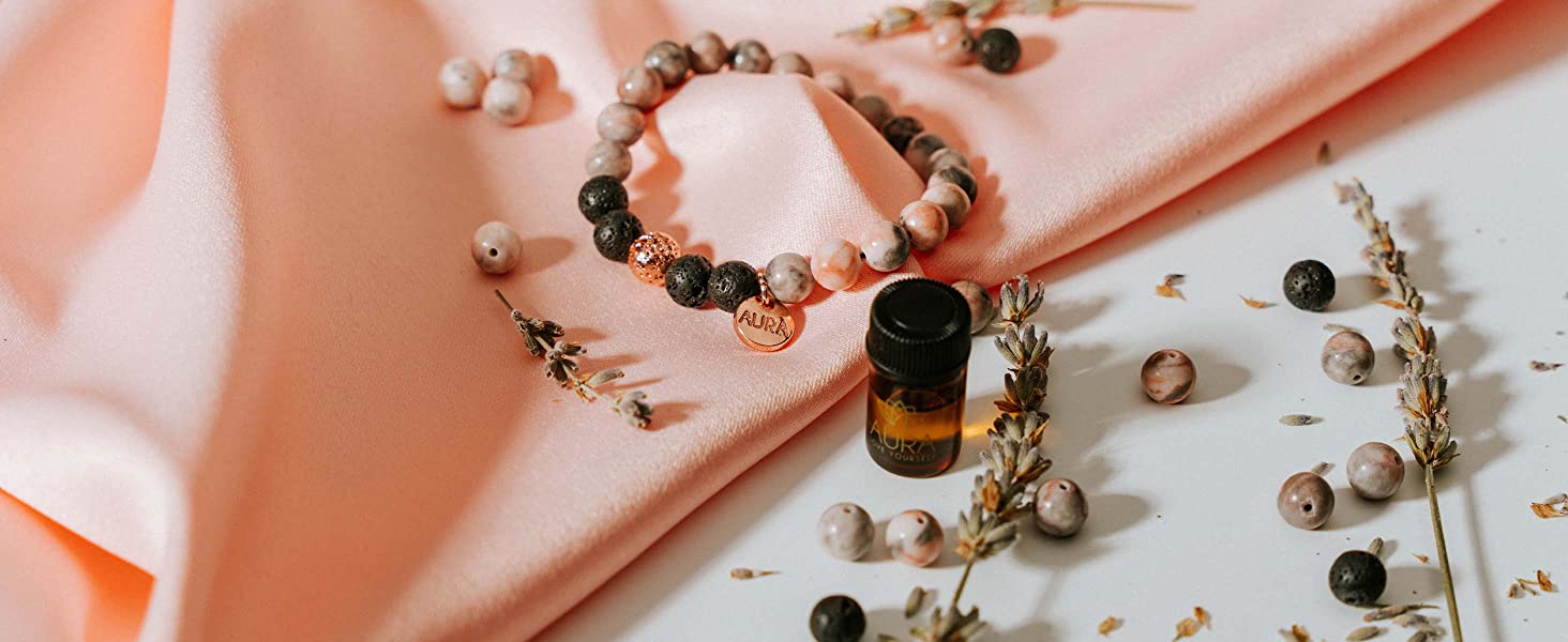 stylized studio shot of aura lava rock beaded bracelet and essential lavender oil