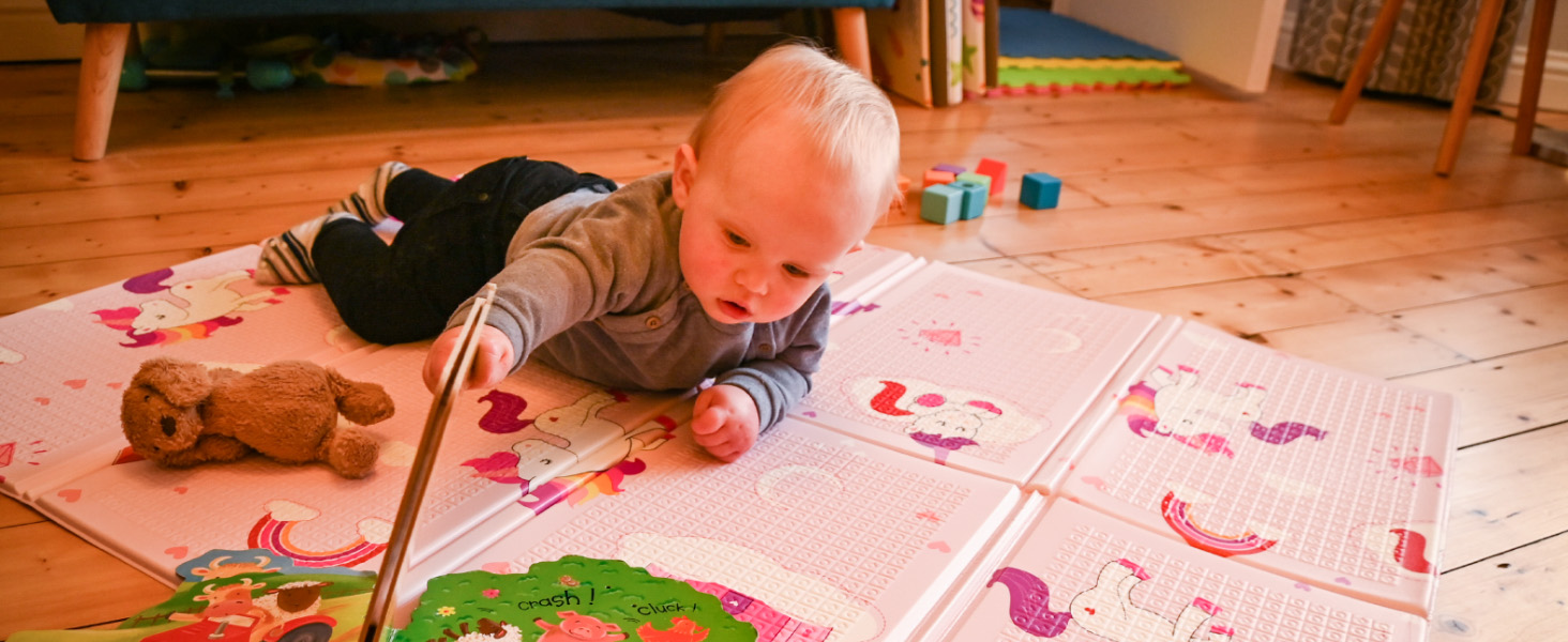 a young boy plays on a pink unicorn print nursery mat