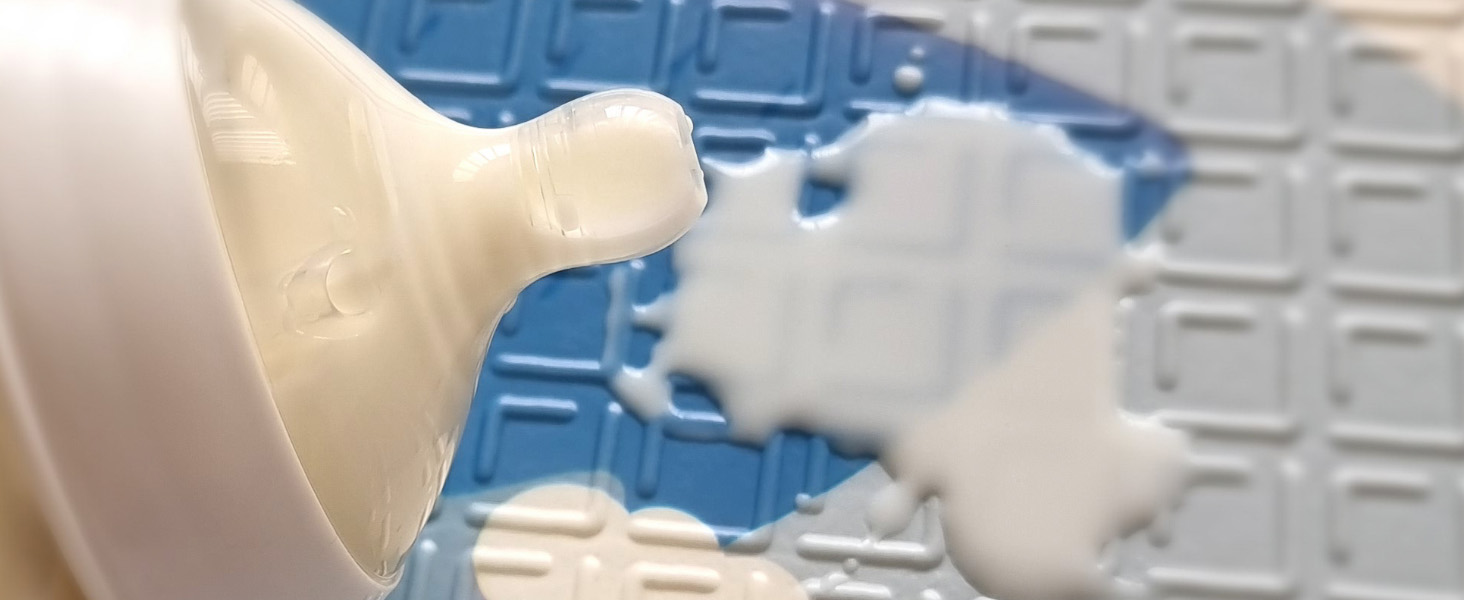 close up of a baby's milk bottle spilt on a blue tummy time mat