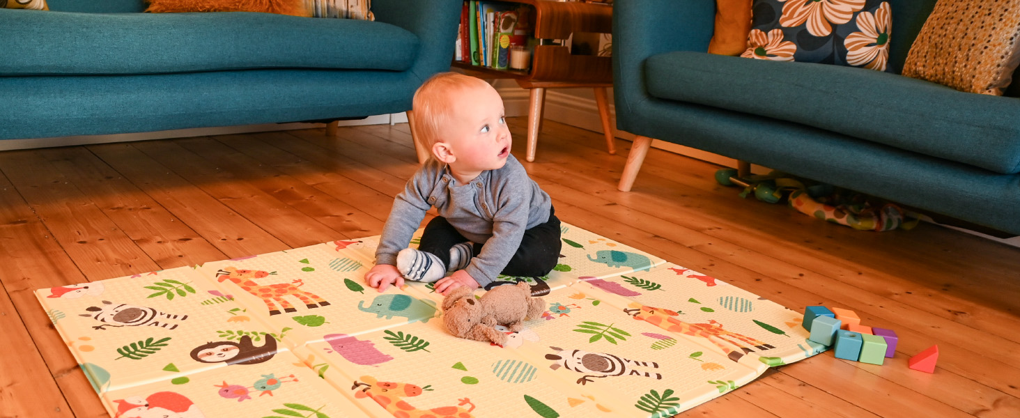 a young toddler plays on an wild animal print nursery mat
