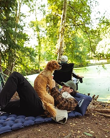 A man and his dog relax together on a TREKKOUT sleeping pad while camping.
