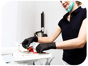 Professional nail care setup showing hands wearing black gloves using nail care equipment on a white surface with visible tools and implements.