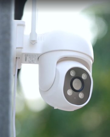 Black outdoor security camera with dual antennas, mounted under an overhang. Features multiple visible lenses and 'GNCC' branding on its cylindrical body.
