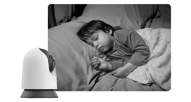 Black and white image showing someone sleeping next to what appears to be a home assistant device or smart speaker.