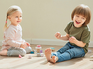 Two young children sitting on the floor playing with wooden toy kitchen utensils and pots, demonstrating educational playtime products.