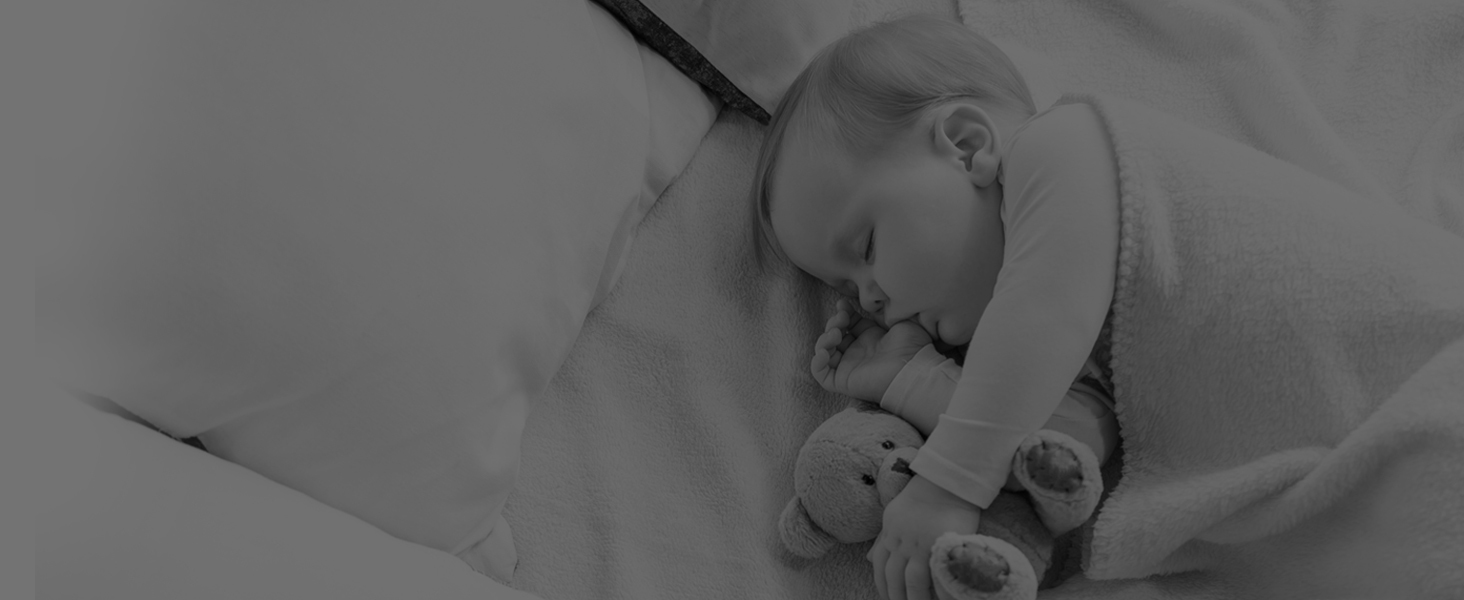Black and white image of a sleeping infant nestled in soft bedding.