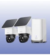 Compact security camera with solar panel attachment on top, mounted against blue gradient background. White dome housing with black mounting bracket visible.