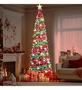 Tall, slim blue pre-lit Christmas tree in living room corner, illuminated with warm white lights. Stockings hang from decorated mantel with wreath and candles.