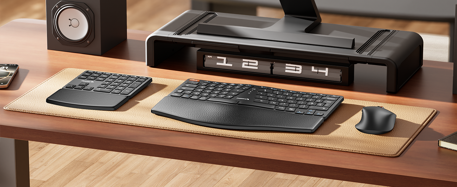 Ergonomic desk setup with split keyboard, mouse, and numeric keypad on a textured mat. Large black monitor stand with digital display above.