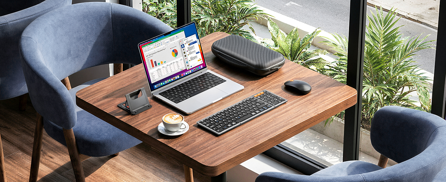 Wooden desk workspace with laptop, headphones, notebook, and plant. Person wearing blue long-sleeve shirt working at desk near window with natural outdoor lighting.