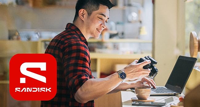 Text shows 'SANDISK' logo in red and white. Image shows person in plaid shirt working at laptop with electronic device in hand.