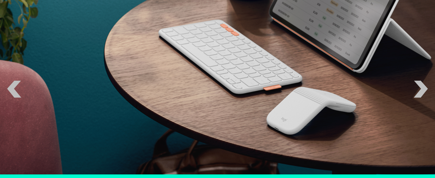 White computer mouse positioned on wooden round table surface next to laptop keyboard in indoor setting with teal wall background.