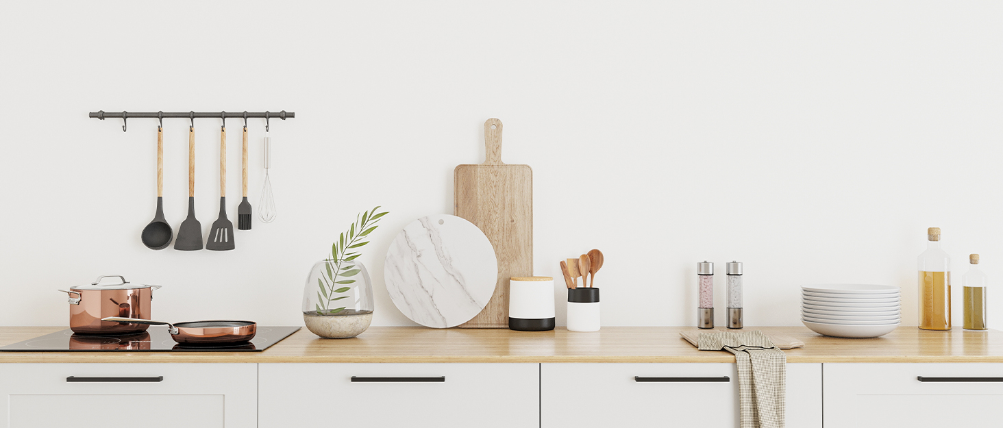 Kitchen countertop styling featuring hanging utensils on rail, wooden cutting board, white plates, glass jars with dried goods, potted plant, and wooden spoon on neutral background.