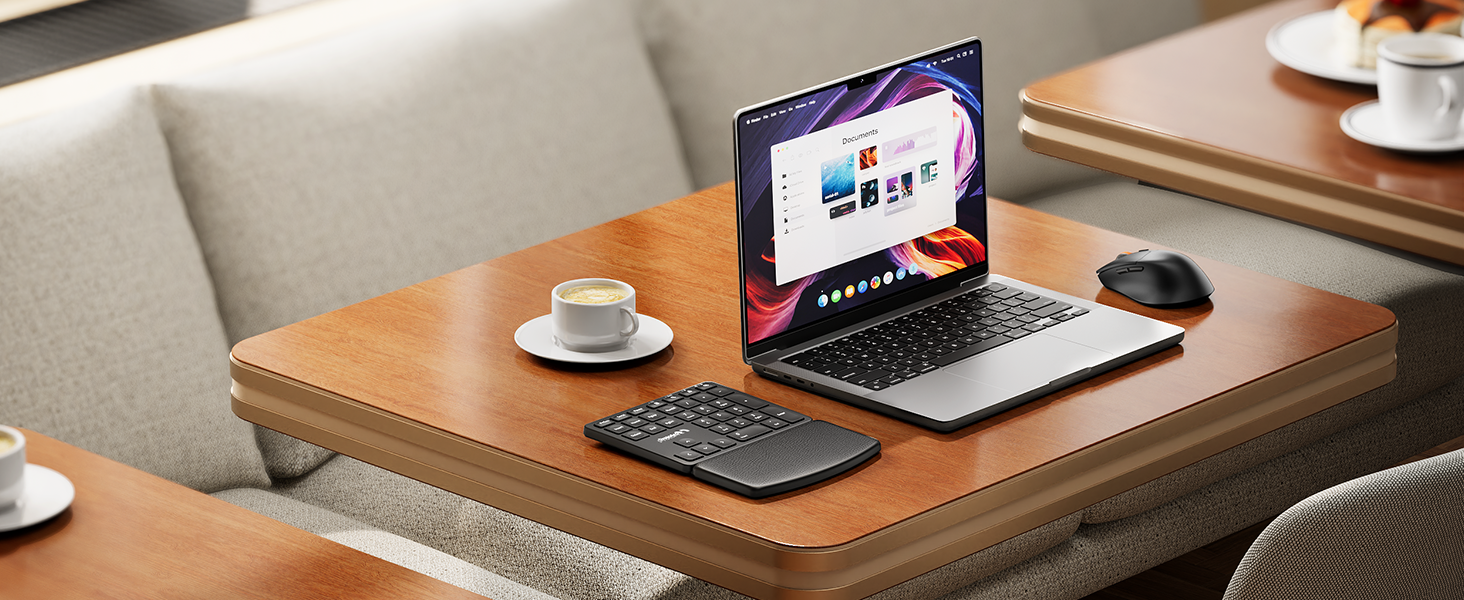 Sleek laptop on wooden desk displaying colorful interface. External keyboard and mouse nearby. Coffee cups and notebook visible, suggesting work environment.
