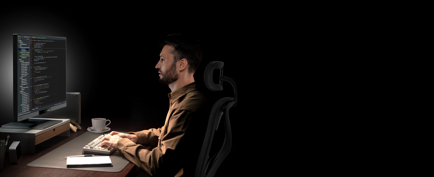 Person working at desk in dark environment with computer monitors displaying design software interface.