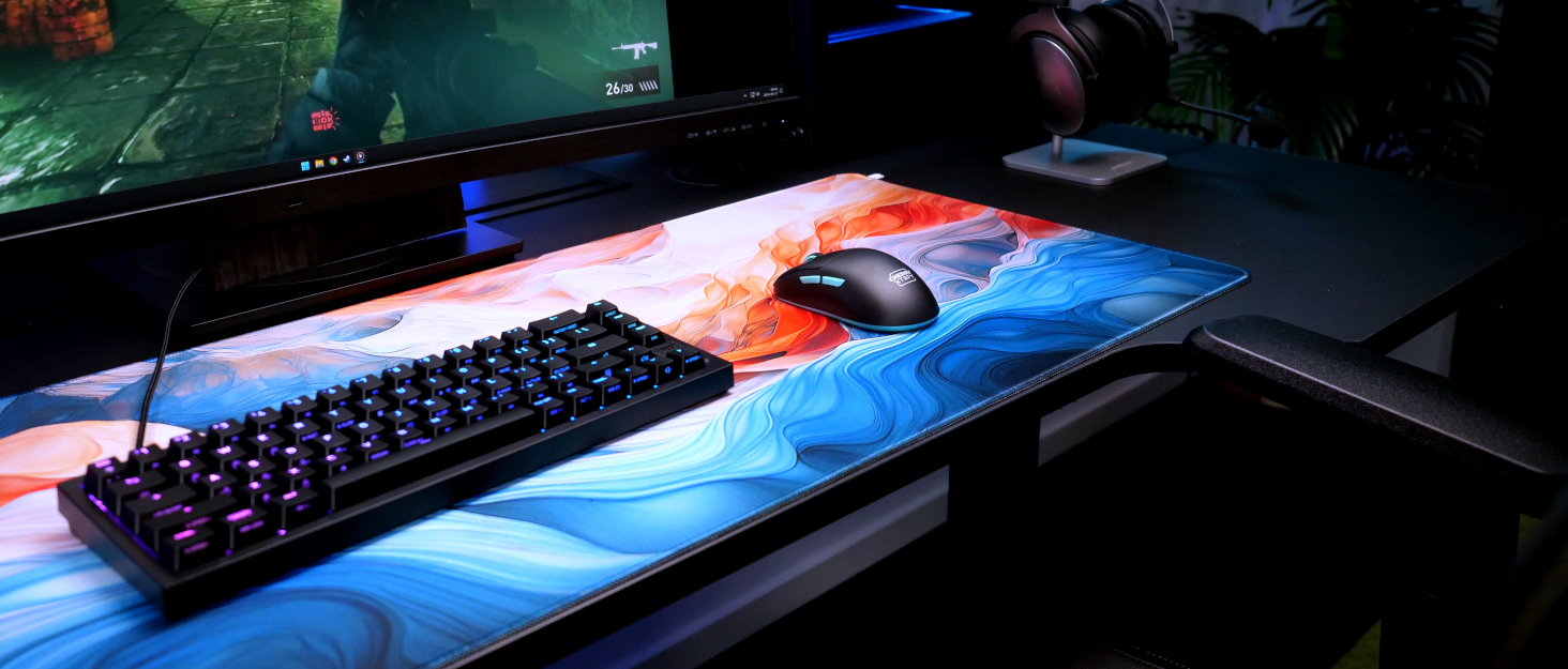 Extended RGB mousepad with vibrant red and blue wave pattern design across its surface. Black gaming keyboard and mouse visible on the pad.
