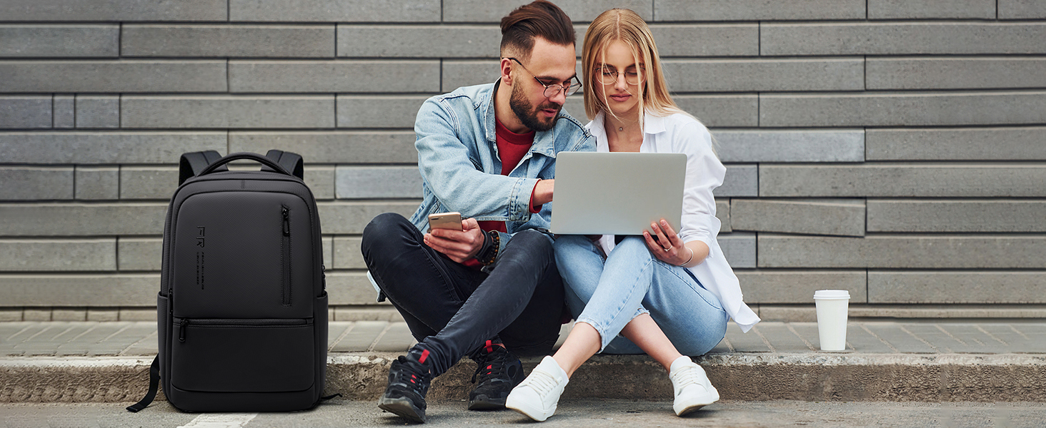 Couple sitting outdoors against brick wall reviewing document on laptop together in casual seated position.