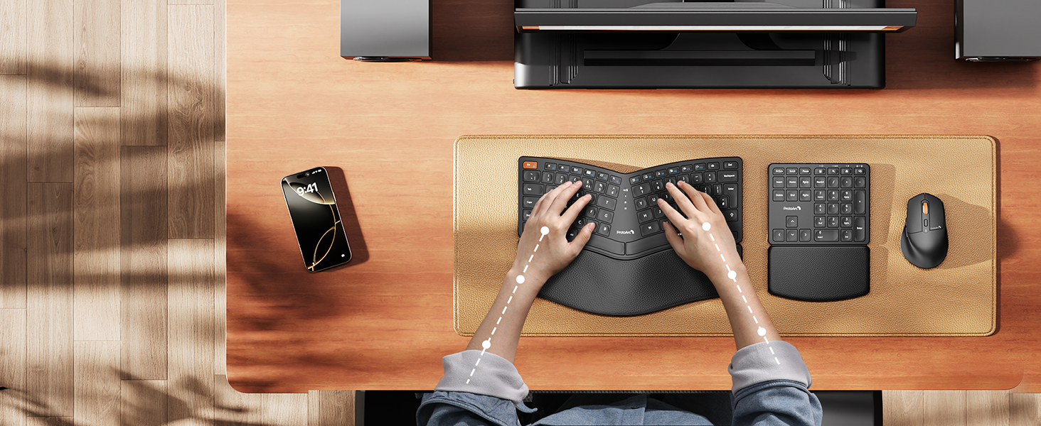 Overhead view of desk workspace with ergonomic keyboard, wireless mouse, numeric keypad, and smartphone. Hands positioned on keyboard, demonstrating ergonomic typing posture.