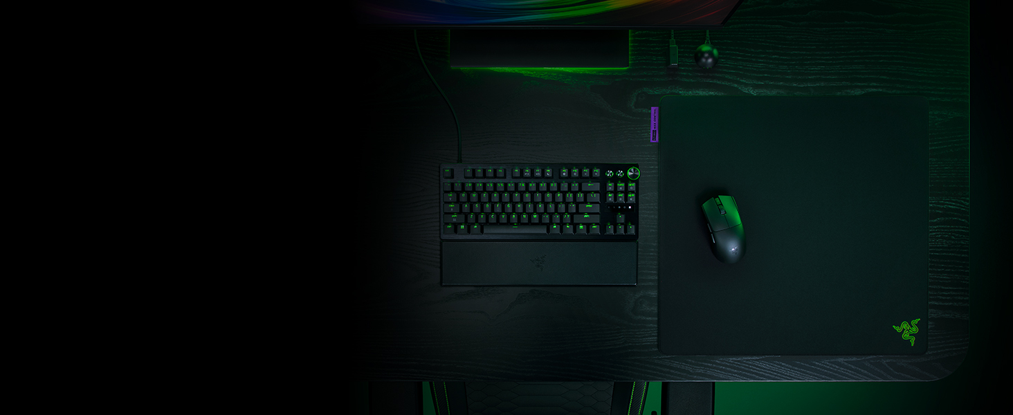 Dark computer setup with illuminated gaming peripherals, featuring multiple monitors and RGB lighting effects.