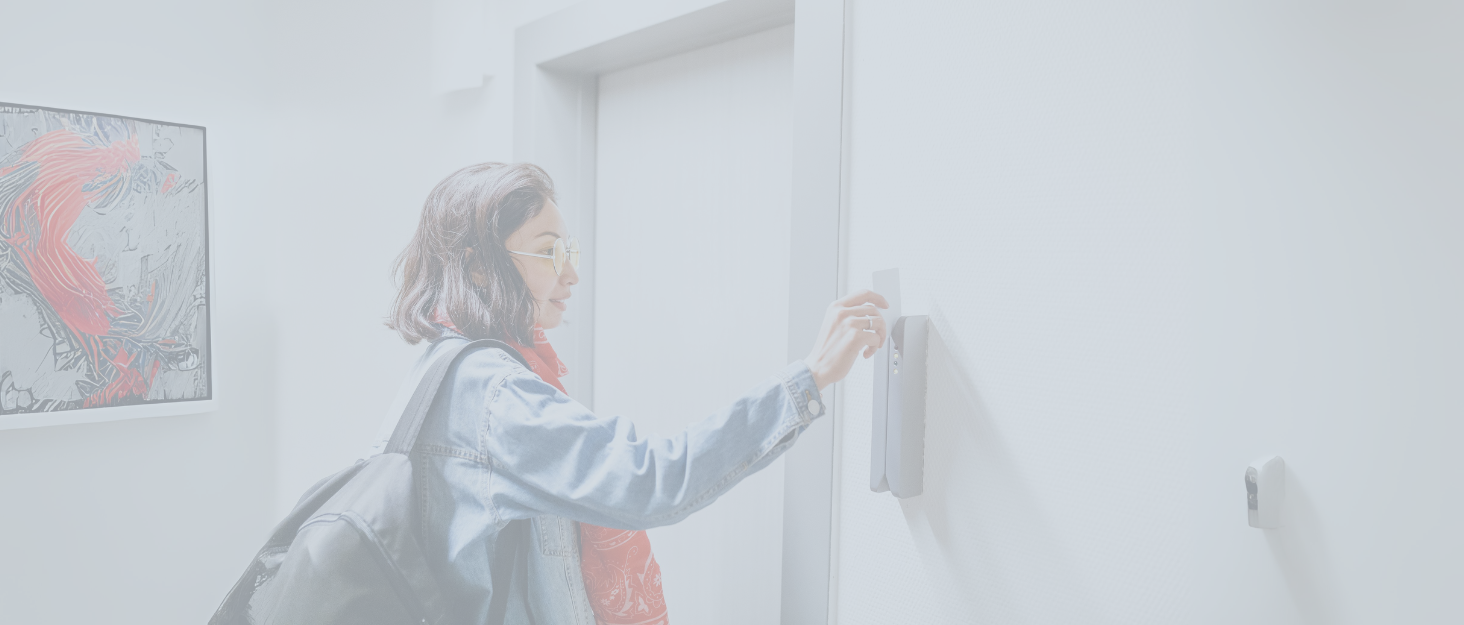 Woman in blue shirt using a smart home device or light switch on a white wall in a minimalist interior setting.