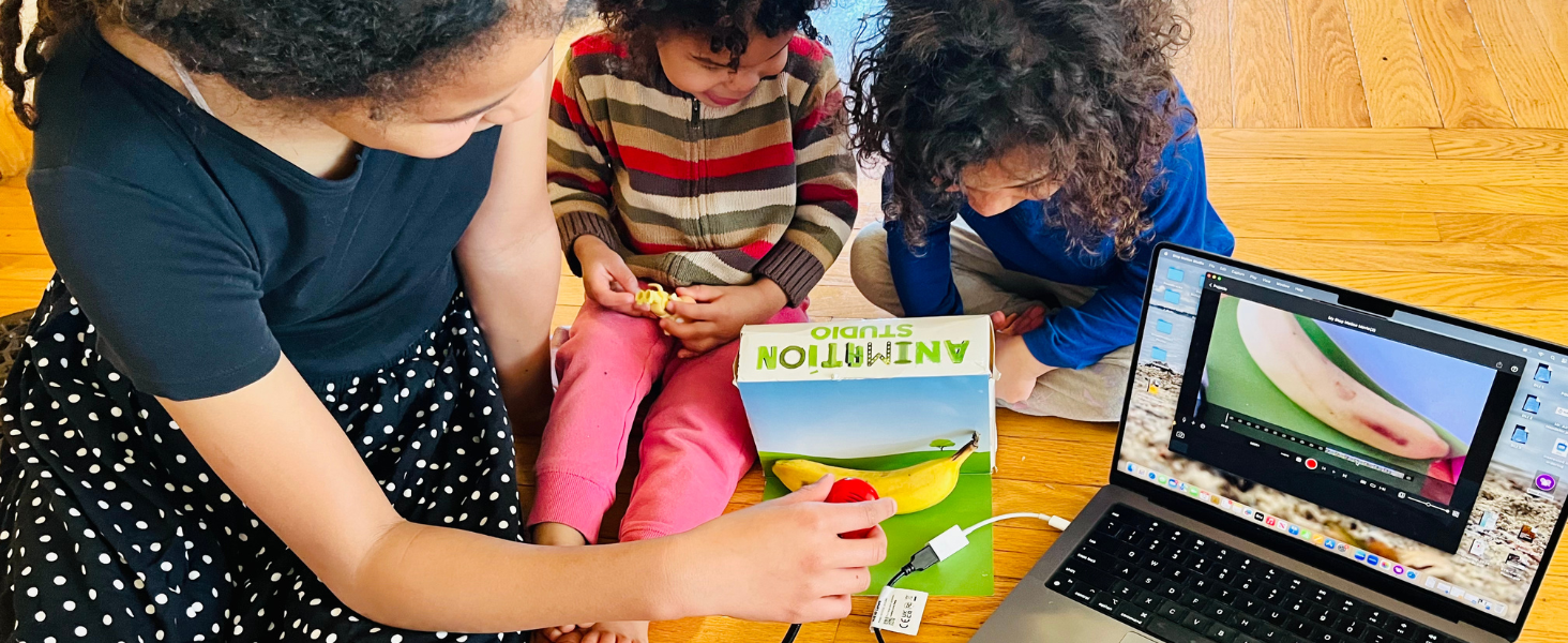 Children engaged in creative activities at table with craft supplies, toys, educational materials, and laptop computer visible.