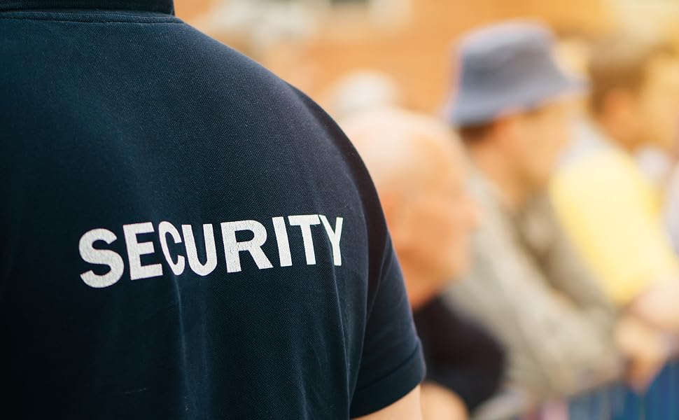 Text reads 'SECURITY'. Close-up of person wearing dark navy jacket with white embroidered security text, blurred background with crowd.