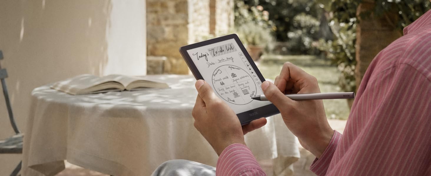 Person holding e-reader device with visible display screen, shown being used in casual home setting near window with plants.