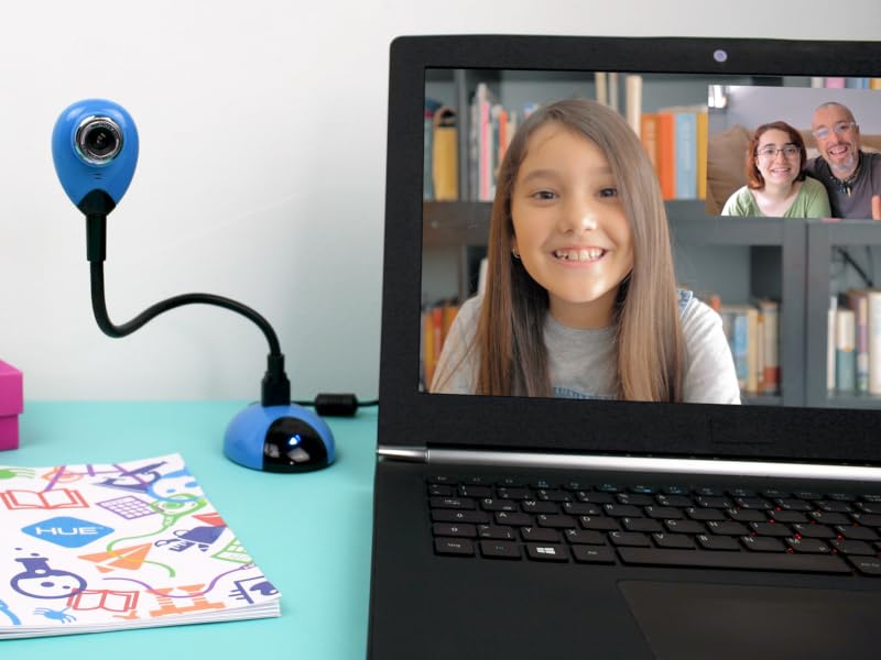 Laptop displaying video call with blue webcam attached. Colorful school supplies visible on desk, showcasing online learning setup.