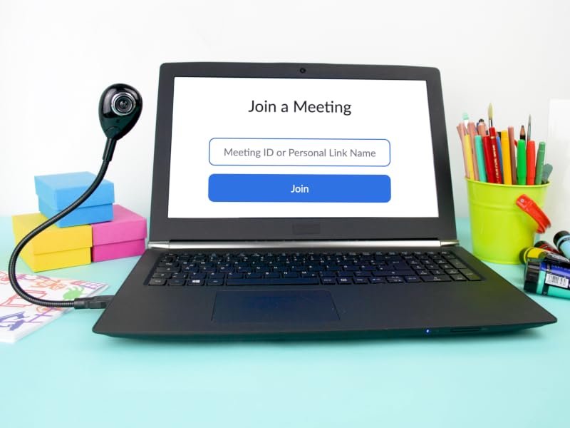 Laptop on desk with 'Join a Meeting' screen, surrounded by office supplies including colorful pencils, a small webcam, and sticky notes.