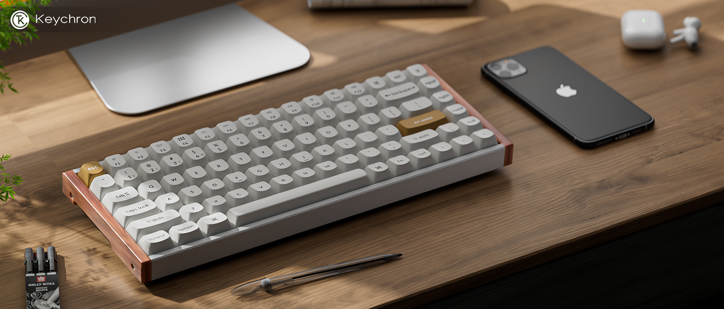 Mechanical keyboard with white keycaps and wood accent on a wooden desk, alongside a black smartphone and partial view of a silver monitor or laptop.