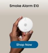 Text reads 'Motion Sensor E20' and 'Shop Now'. White motion sensor device held in person's hand against neutral background.
