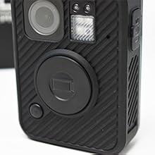 Black and yellow body camera with carbon fiber texture. Wide-angle lens, LED indicators, control buttons on sides. Professional-grade portable recording device for law enforcement use.